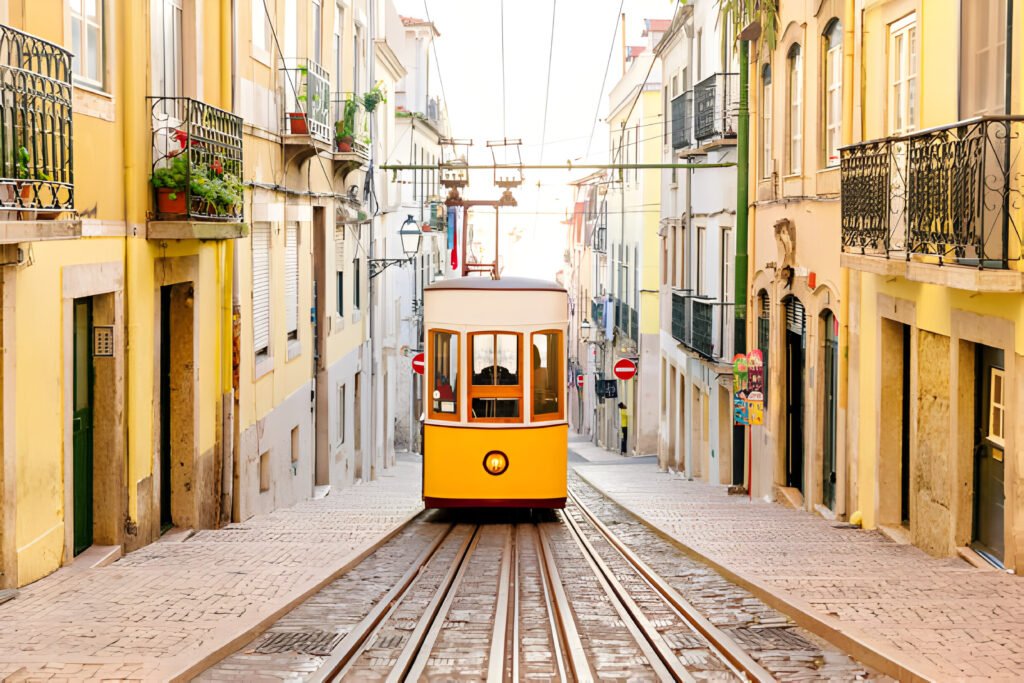 !<Elevador da Bica funicular in Lisbon, Portugal. The image showcases the iconic yellow tram navigating through a narrow, picturesque street lined with colorful buildings. Digital Nomad Visa 2024.